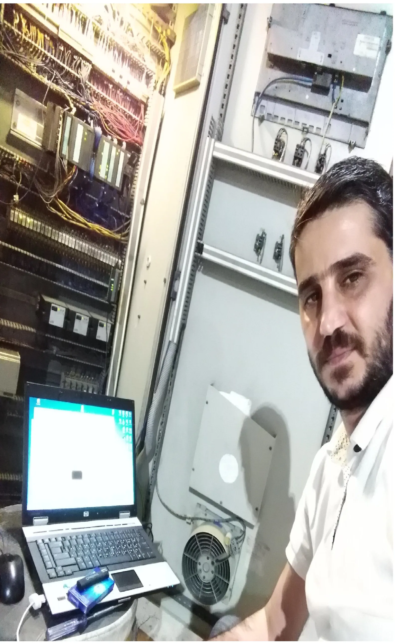 Engineer beside a Siemens control cabinet with a programming laptop